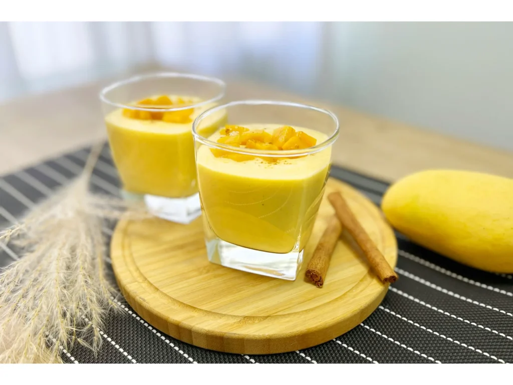 A vibrant mango smoothie, its golden hue shimmering in the warm morning light. In the foreground, a tall glass filled with the creamy, blended fruit, garnished with a sprig of fresh mint. The middle ground showcases an array of superfood add-ins: flaxseeds, chia seeds, and a sprinkle of cinnamon, all providing a nutritious boost to the refreshing beverage. In the background, lush, tropical foliage sets the scene, hinting at the luscious flavors to come. The composition is captured with a wide-angle lens, creating a sense of depth and inviting the viewer to imagine the smooth, velvety texture and tantalizing aroma of this nourishing mango smoothie. A vibrant mango smoothie, its golden hue shimmering in the warm morning light.