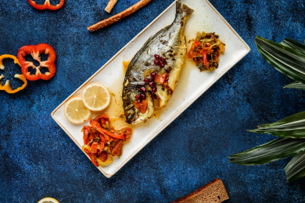 Image of a perfectly roasted whole branzino with herbs and lemon slices on a baking sheet. Branzino 101