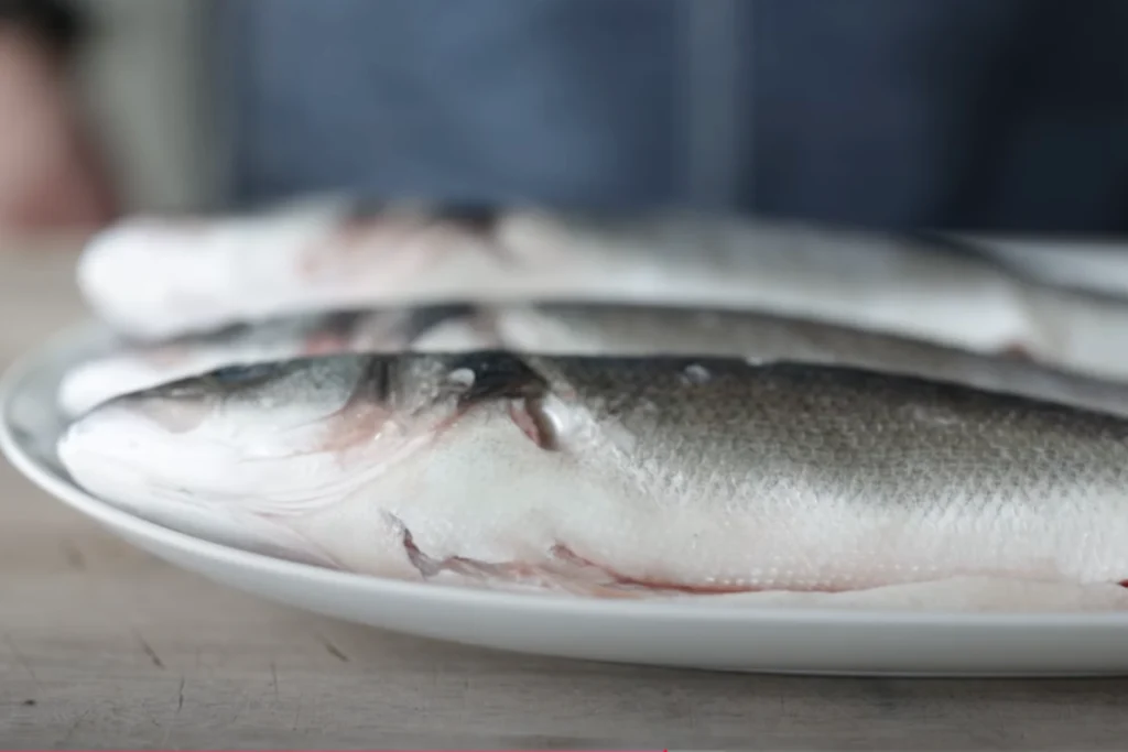 A pristine, well-lit kitchen counter showcases a neatly arranged spread of fresh branzino filets. The fish fillets, their skin glistening with a subtle sheen, are accompanied by a collection of essential mise en place: a sharp fillet knife, a wooden cutting board, fresh lemon wedges, a sprinkle of sea salt, and a drizzle of high-quality olive oil. The overall scene exudes a sense of culinary precision and attention to detail, perfectly capturing the essence of "Preparing Branzino for Cooking".