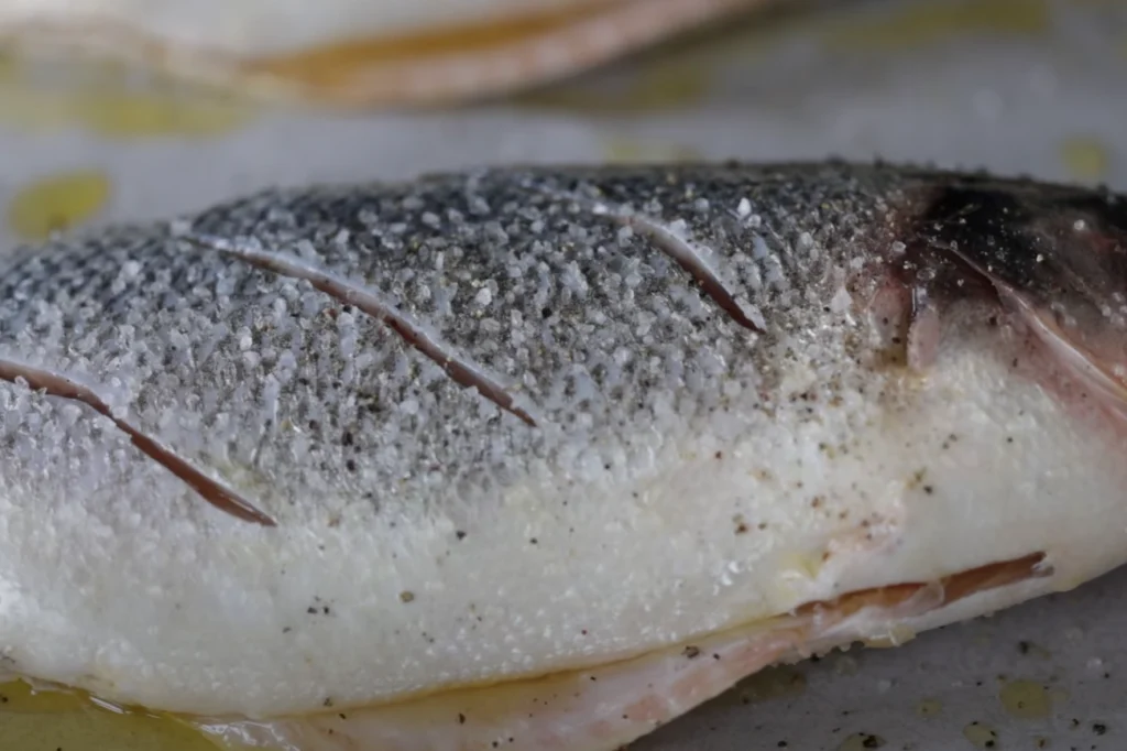 A still life arrangement featuring an assortment of fresh branzino fish fillets, seasoned with a variety of aromatic spices and herbs. In the foreground, the fish fillets are arranged in a visually appealing manner, highlighting their delicate texture and natural colors. The middle ground showcases the spice blend, with piles of crushed peppercorns, dried oregano, lemon zest, and sea salt. The background features a wooden cutting board or rustic table surface, creating a warm, earthy atmosphere. The lighting is soft and diffused, casting gentle shadows and highlighting the details of the ingredients. The overall composition conveys the idea of a flavorful, thoughtfully-prepared branzino dish, ready to be enjoyed. Branzino
