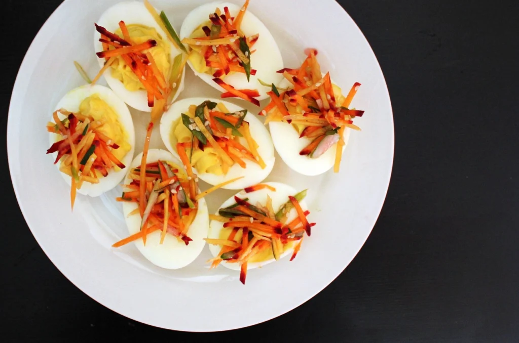 A neatly arranged composition showcasing the essential ingredients for perfect deviled eggs - hard-boiled eggs, mayonnaise, Dijon mustard, paprika, and chives. The items are artfully placed on a rustic wooden surface, with natural lighting accentuating their textures and colors. The scene exudes a cozy, homemade atmosphere, inviting the viewer to imagine the delicious flavors. The camera captures the ingredients from a slightly elevated angle, creating a visually appealing and appetizing display.