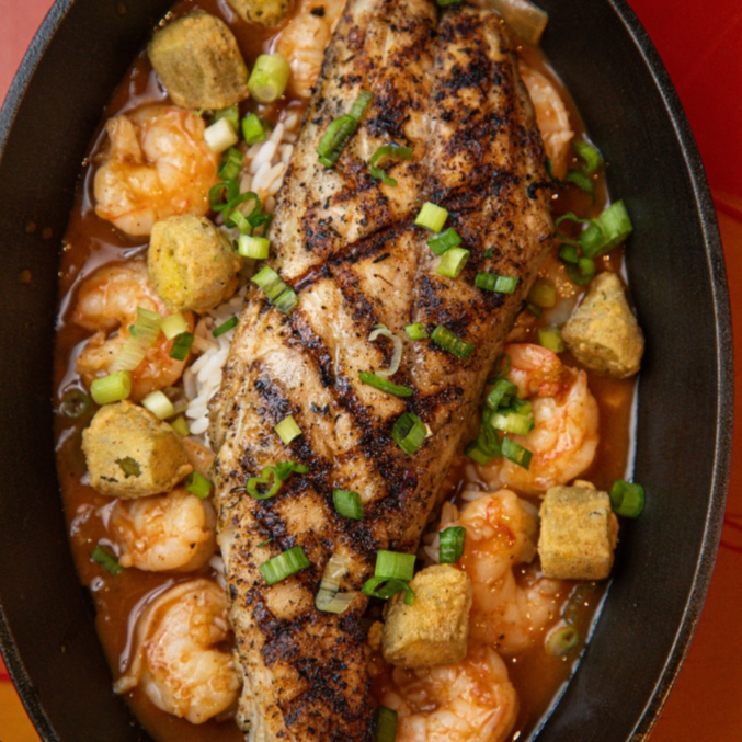 A cast iron skillet rests on a rustic wooden surface, the center filled with a beautifully blackened redfish fillet. The fish's crisp, charred exterior contrasts with the moist, flaky interior, a testament to the intense heat and seasoning. Sizzling oil glistens around the edges, adding a tempting aroma. Warm, soft lighting casts a golden glow, highlighting the skillet's weathered texture and the fish's rich, reddish-brown hues. The scene conveys a sense of comfort and culinary expertise, inviting the viewer to imagine the savory flavors and satisfying texture of this perfectly cooked blackened redfish. redfish on the grill