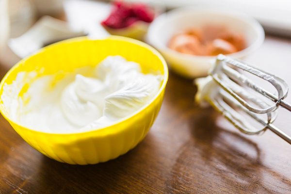 A close-up view of a smooth, creamy lemon mascarpone dessert, with a silky, pale yellow texture. The foreground features the rich, decadent cream, dolloped neatly onto a pristine, white ceramic plate. Soft, natural lighting casts a warm, diffused glow, accentuating the luxurious, velvety finish. In the middle ground, delicate, edible flowers in shades of yellow and white add a delicate, aromatic accent. The background is blurred, allowing the focus to remain solely on the luscious, citrus-infused cream, creating an elegant, appetizing composition.